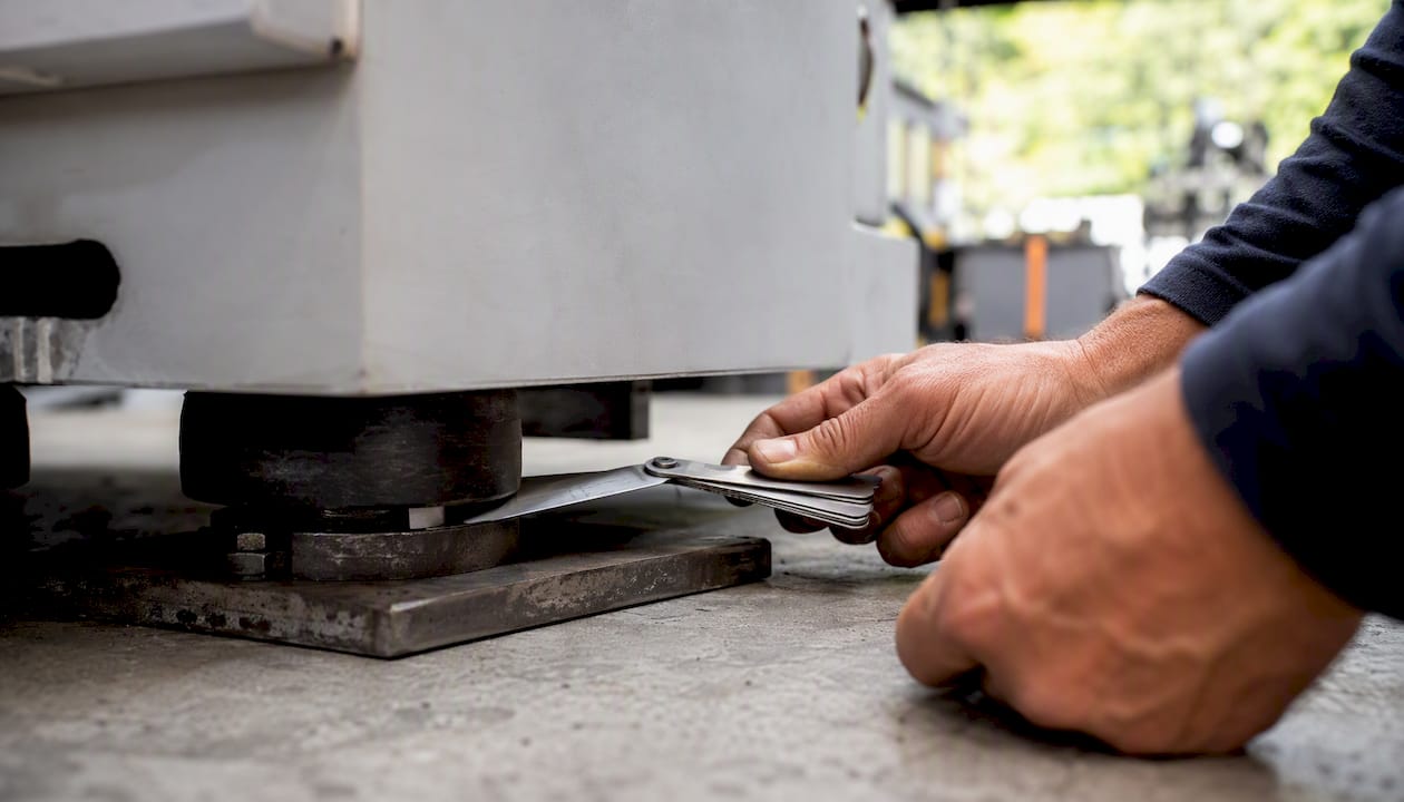 Hands checking CNC machine foot with feeler gauges